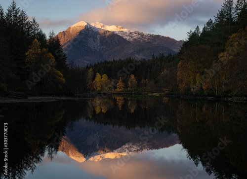 Lochan Glencoe with in the background the mountains with snow in the tops and the first light of sunrise. Photo taken during windless weather with a perfect reflection. 