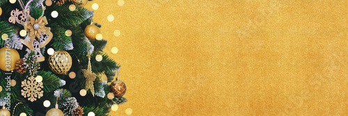 Golden holidays banner with decorated Christmas tree branches and bright bokeh. New Year background with copy space. 
