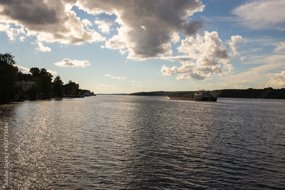 The sun's rays break through the clouds and illuminate the Volga on which the barge sails. Ivanovo region, Russia. The sun's rays break through the clouds and illuminate the Volga on which the barge sails. Ivanovo region, Russia.