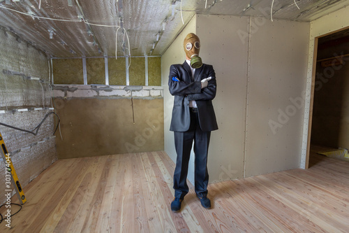 Strange man in businessman suit and gas protection mask inside a room under renovation works.