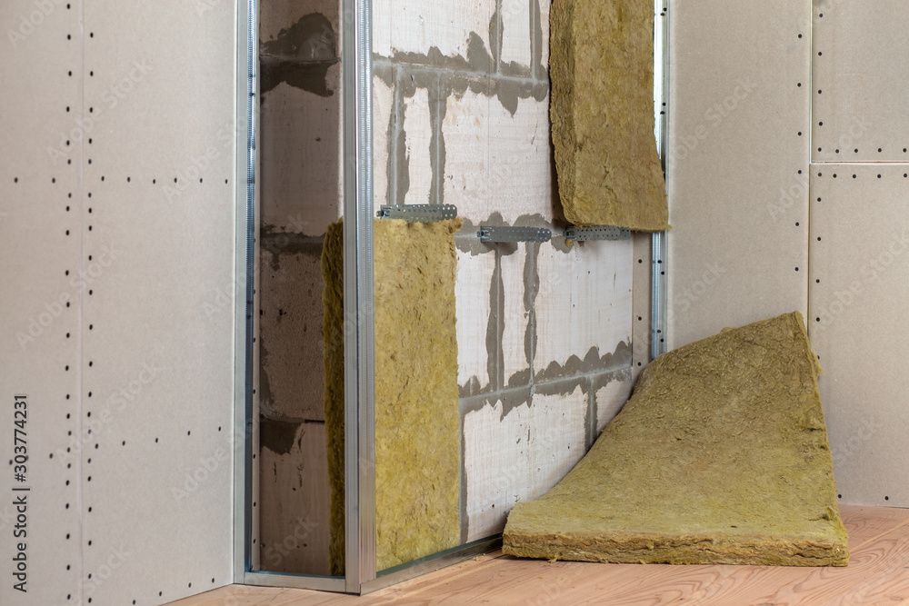 Wall of a room under renovation with mineral rock wool insulation and metal frame prepared for drywall plates.