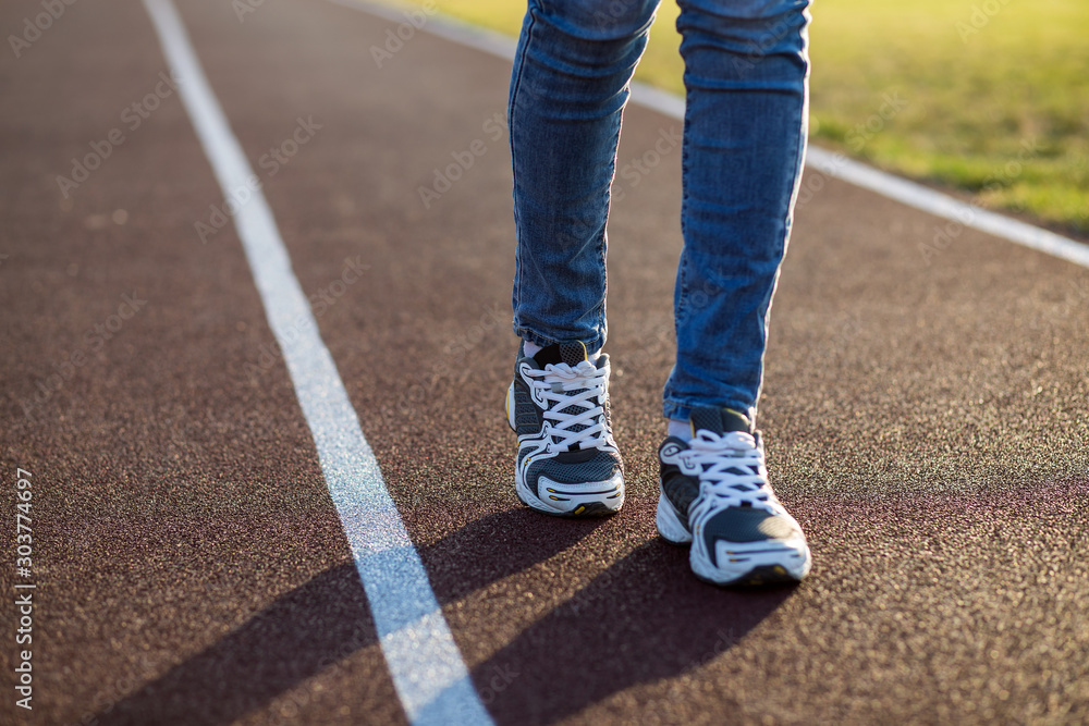 Close up of woman feet in sport sneakers and blue jeans on running lane on outdoor sports court. Close up of woman feet in sport sneakers and blue jeans on running lane on outdoor sports court.