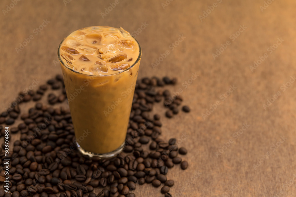 A glass of iced coffee with coffee beans on brown wooden background A glass of iced coffee with coffee beans on brown wooden background