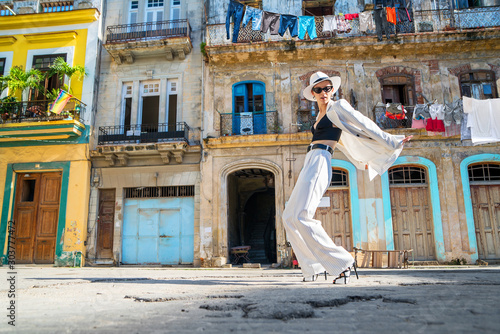 Photography Stylish woman in a white suit and white hat dancing on an city street of Cuba