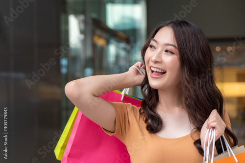 happy smiling woman shopping with colorful shopping bag in shopping mall or shopping center; concept of buying, grand sale, boxing day, celebration sale, discount, good deal for woman shoppers