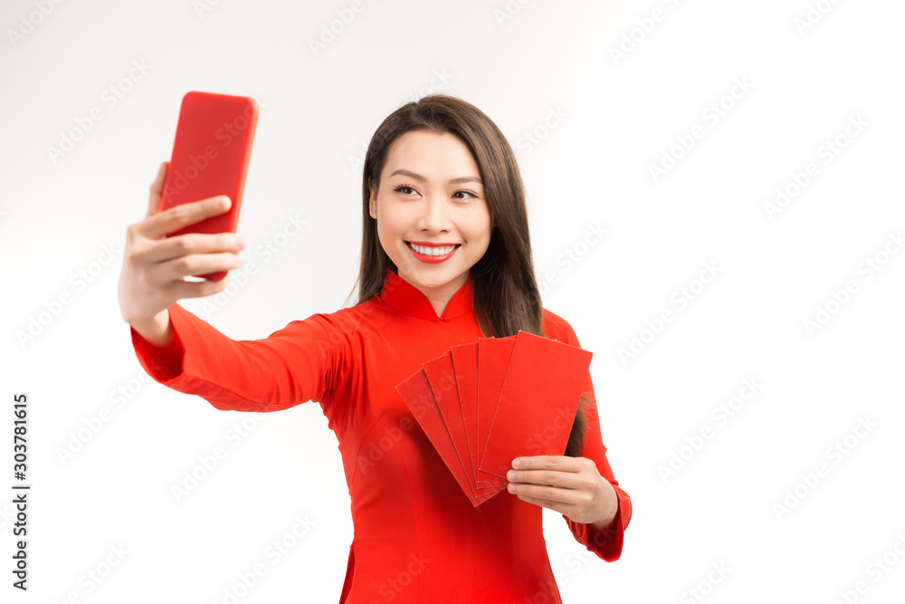 Smiling Vietnamese woman taking selfie by mobile phone with red envelopes against white background Smiling Vietnamese woman taking selfie by mobile phone with red envelopes against white background