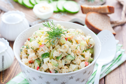 Salad with crab sticks, fresh cucumbers and rice in a white bowl, horizontal