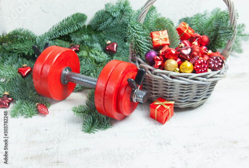 Christmas or New Year on a white background. Composition with dumbbells, gift, red glass balls, fir tree branches for healthy lifestyle and sport