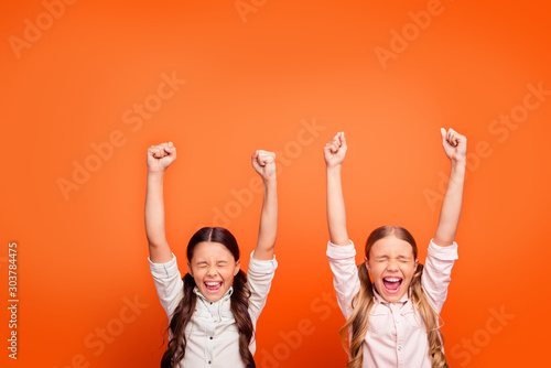 Yeah unbelievable victory. Portrait of lucky delighted crazy two kids girls win contest feel euphoria scream raise fists wear modern clothing isolated orange color background