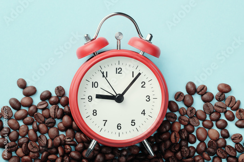 Red alarm clock and roasted coffee beans on blue background. Concept of morning awakening, beginning of working day photo