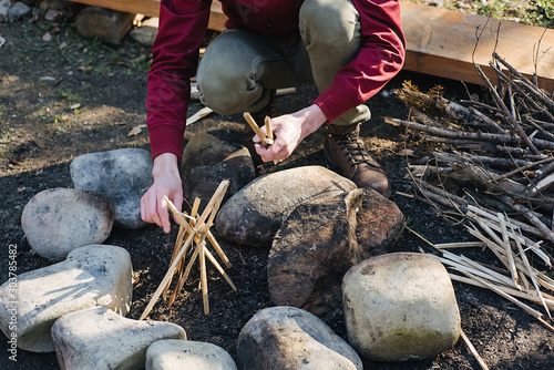 Close up young hiker male prepare brunches for bonfire in forest. Traveler bearded man, making campfire after trekking. Explore travel real wilderness lifestyle