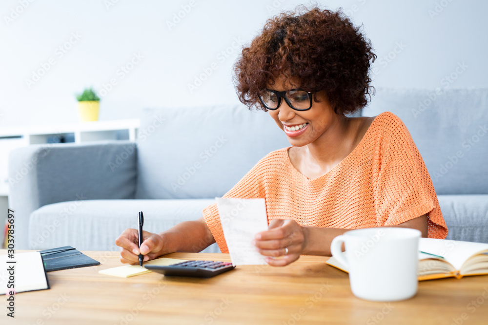 Young woman sitting taking care of bills and home finances while sitting in living room - obrazy, fototapety, plakaty 