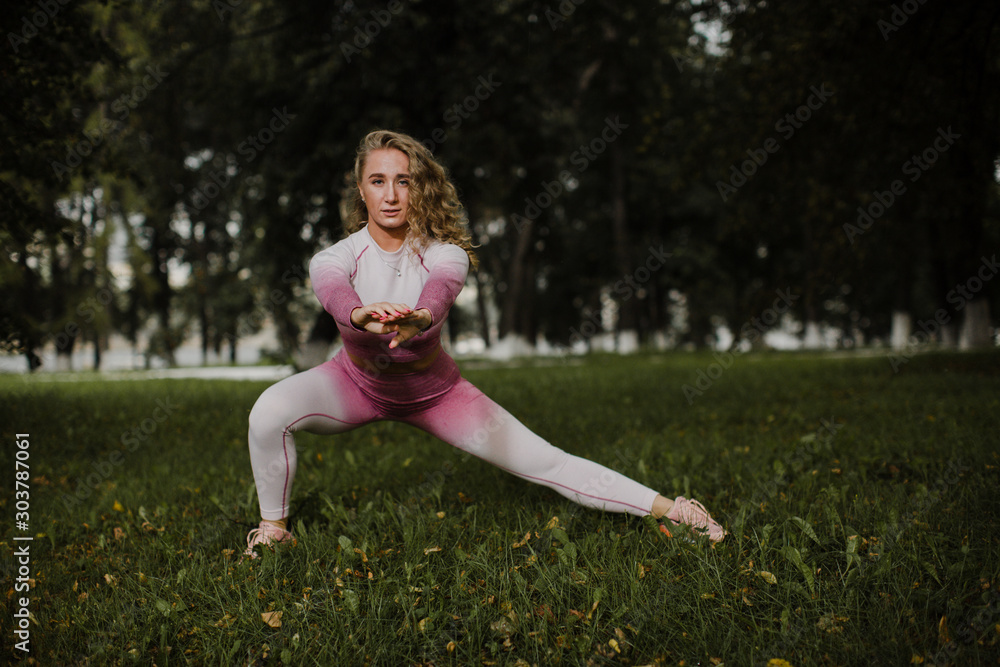 Fototapeta premium Beautiful girl doing squats and stretching on the lawn in the Park.