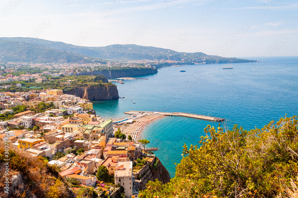 Panorama of high cliffs, Tyrrhenian sea bay with pure azure water, floating boats and ships, pebble beaches, rocky surroundings of Meta, Sant'Agnello and Sorrento cities near Naples region