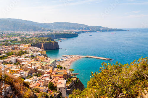 Panorama of high cliffs, Tyrrhenian sea bay with pure azure water, floating boats and ships, pebble beaches, rocky surroundings of Meta, Sant'Agnello and Sorrento cities near Naples region