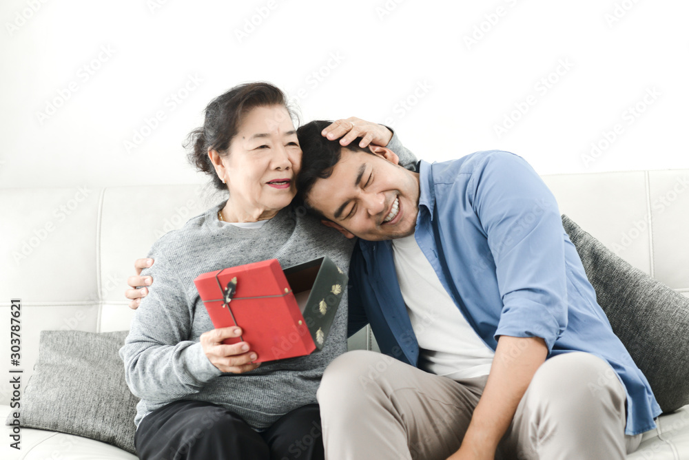 Happy Asian man giving gift box to his mother for Mother's Day celebration. Happy Asian man giving gift box to his mother for Mother's Day celebration.