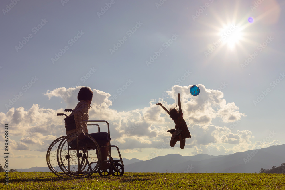 Φωτογραφία Disabled handicapped young girl is sitting on wheelchair and little girl jumping playing with colored balloons at sunset
