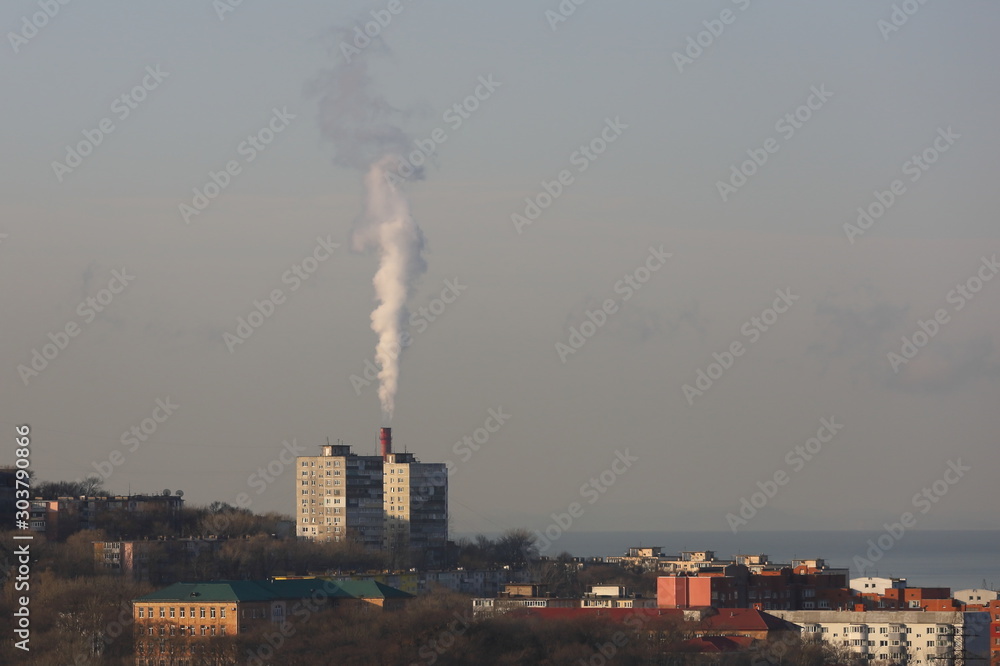 City district with big factory chimney smoking with white smoke. Vladivostok, Far East Russia. 