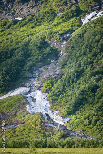 Small waterfall falling down a mountain green side with snow still melting