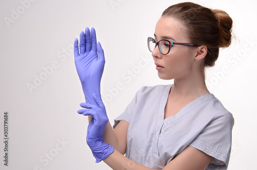 Beautiful female doctor, medical assistant or nurse wearing glasses, putting on latex or rubber gloves on white background. Health care concept. Copy space for your text