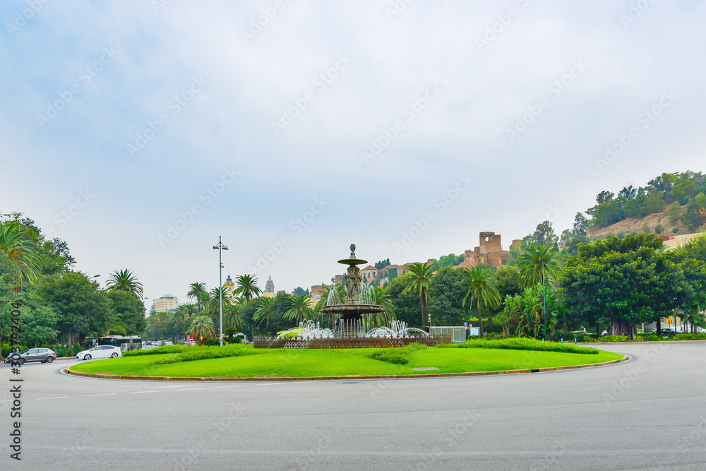A cityscape with a alcazaba and fountain of three graces in a classical style at the roundabout in the historic city center on a bright summer day.