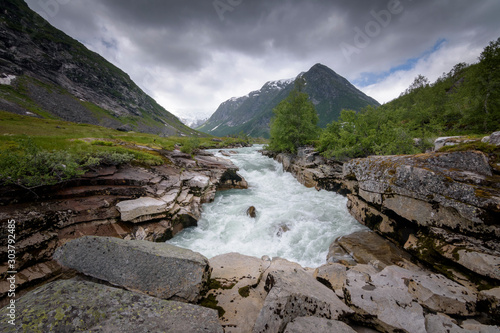 Norwegian green mountain scenery with glacial fed river raging down