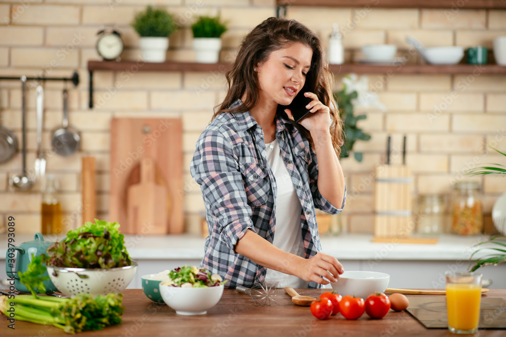 Young woman in kitchen. Beautiful woman taking on phone while cooking.