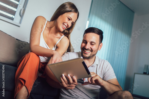Young couple watching media content online in a tablet sitting on a sofa in the living room. © Mediteraneo