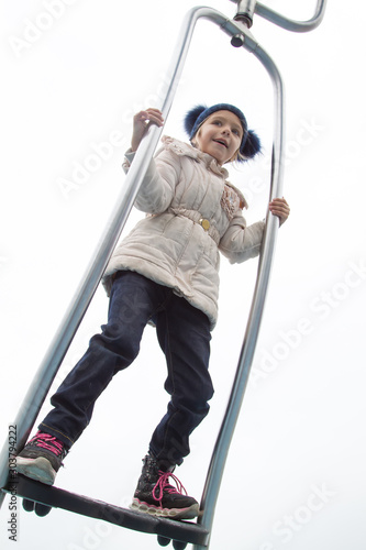 girl in warm clothes spins and balances on modern metal carousel outdoor in autumn