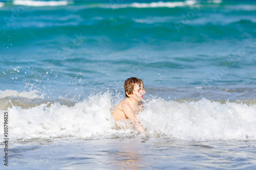 Adorable little blond kid boy having fun on ocean beach. Excited child playing with waves, swimming, splashing and happy about family vacations in Miami, Florida, USA.. © Irina Schmidt