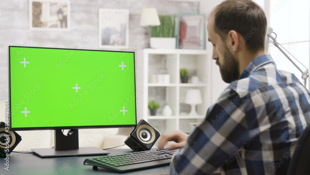 Man looks at green screen PC display in well lit home Man looks at green screen PC display in well lit home