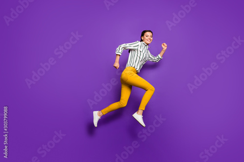Full length profile photo of crazy beautiful lady jumping high rushing discount prices shopping wear striped shirt yellow trousers isolated purple color background