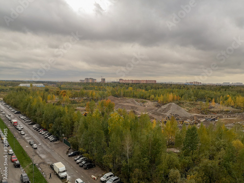 Top view of the road with parked cars and green trees stretching to the horizon with a pile of earth in the middle against a low gray sky with clouds