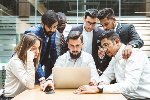 A team of young office workers, businessmen with laptop working at the table, communicating together in an office. Corporate businessteam and manager in a meeting. coworking.