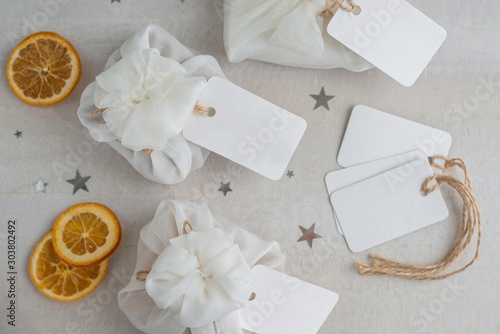 Christmas presents wrapped with white furoshiki fabric, labels and dried orange slices. Eco friendly gift. © Ira_Shpiller
