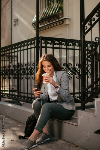 Beautiful businesswoman on coffee break using phone. Young businesswoman outdoors. 
