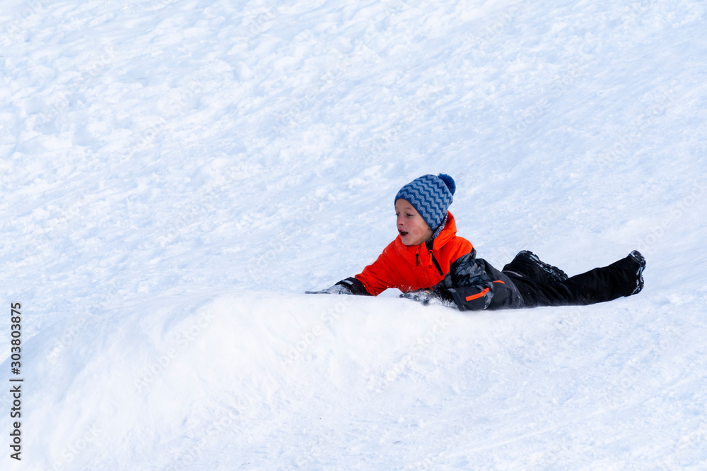 Boy sledding down the hills without sledge on a winter day.