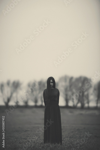 Girl in a long dress on the background of a gloomy forest black and white photo . A woman in a dark forest scary atmosphere like in a horror movie. An image of a girl from a Halloween horror movie.