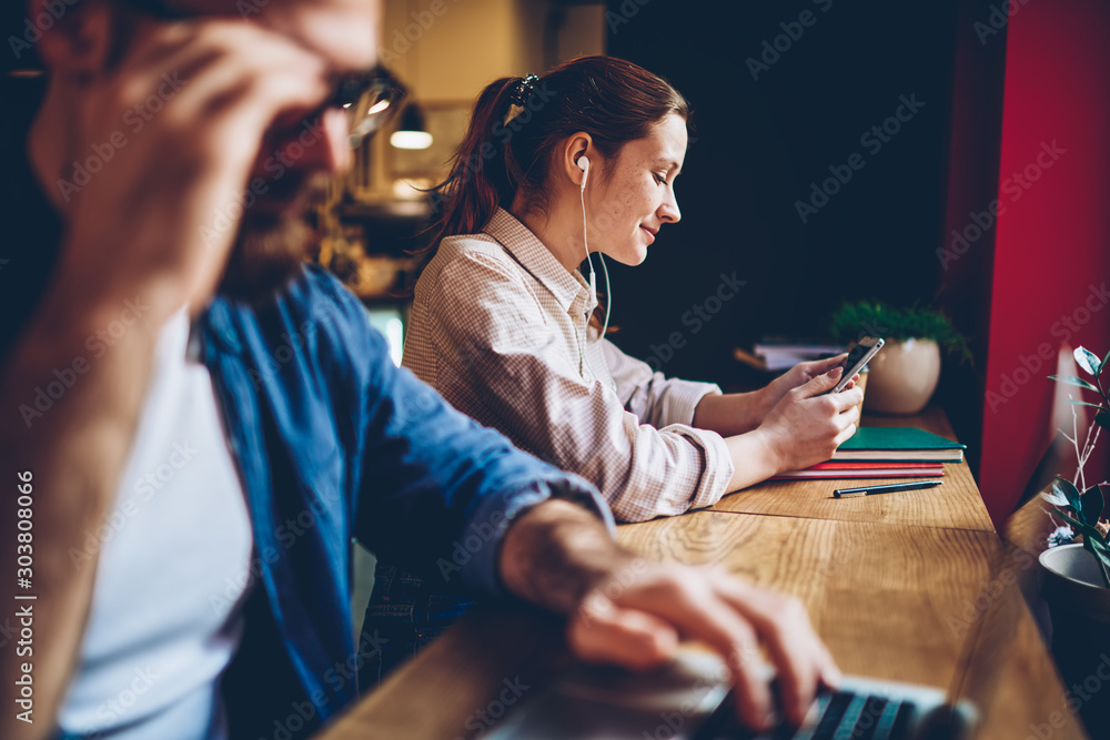 Φωτογραφία Cheerful young woman listening audiobook downloaded on smartphone in modern earphones sitting in coworking