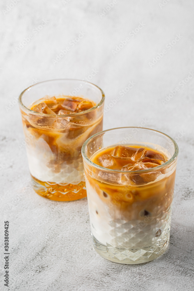 Two glasses with cold brew coffee and milk isolated on bright marble background. Overhead view, copy space. Advertising for cafe menu. Coffee shop menu. Vertical photo. Two glasses with cold brew coffee and milk isolated on bright marble background. Overhead view, copy space. Advertising for cafe menu. Coffee shop menu. Vertical photo.