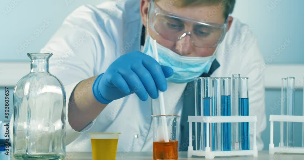 Scientist in the Lab in Blue Gloves and a Mask Analithing Chemical Liquid inside a Flask or Test Tube. Close up 4k footage. Scientist in the Lab in Blue Gloves and a Mask Analithing Chemical Liquid inside a Flask or Test Tube. Close up 4k footage.