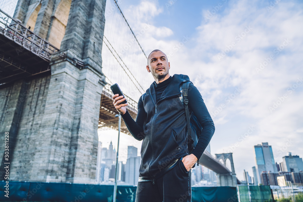 Concentrated shapely male using cellphone near bridge Concentrated shapely male using cellphone near bridge