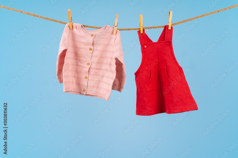 Baby girl clothes pinned on a clothesline against blue background Baby girl clothes pinned on a clothesline against blue background