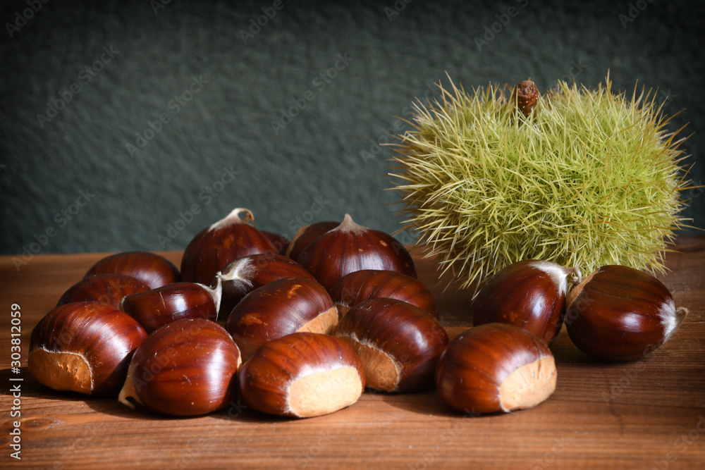 Closeup on chestnuts and curly on wooden background. Raw chestnuts for Christmas. Closeup on chestnuts and curly on wooden background. Raw chestnuts for Christmas.