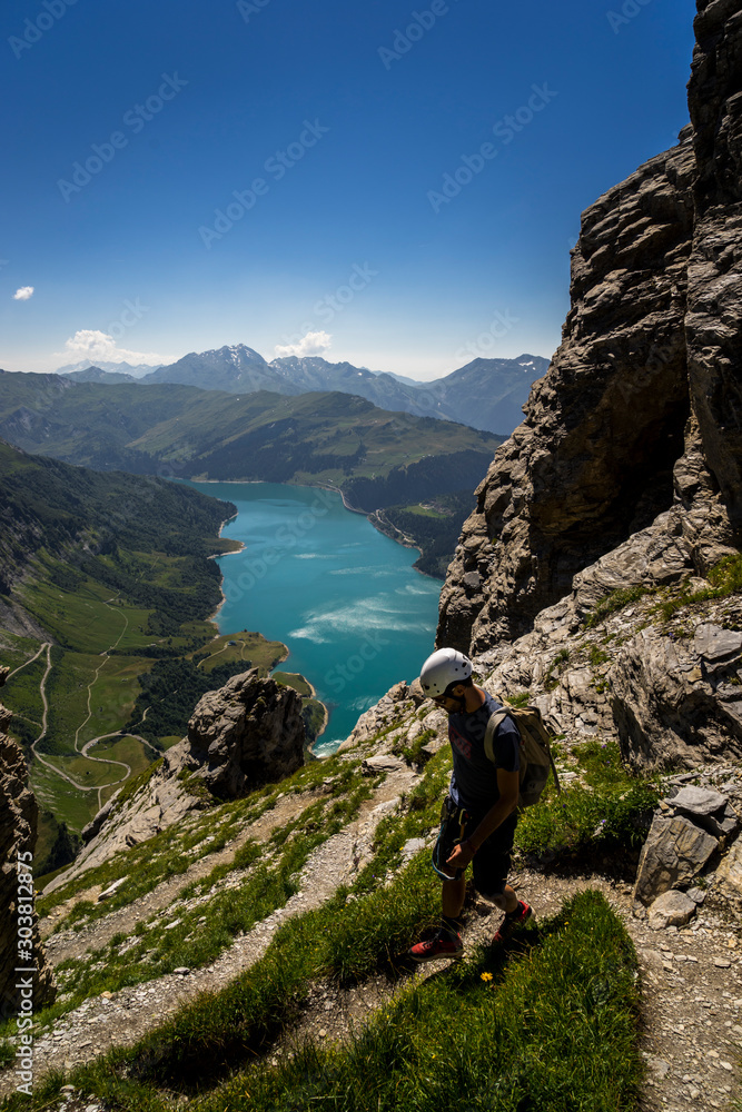 Climber on his way down in the via ferrata Le Roc du Vent, with the Roselend lake and dam in the background - Beaufort, Savoie, France