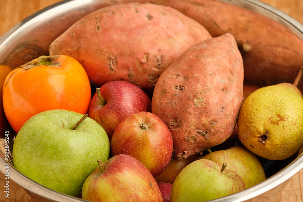 Colorful background with healthy fruits and vegetables like apples, kaki and sweet potatoes lying close together in a silver tin bowl. Colorful background with healthy fruits and vegetables like apples, kaki and sweet potatoes lying close together in a silver tin bowl.
