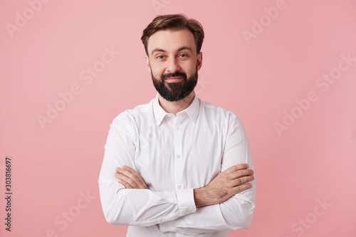 young bearded brunette man male guy with short haircut trendy hairstyle dressed in wearing white shirt formal clothes standing posing isolated over pink background