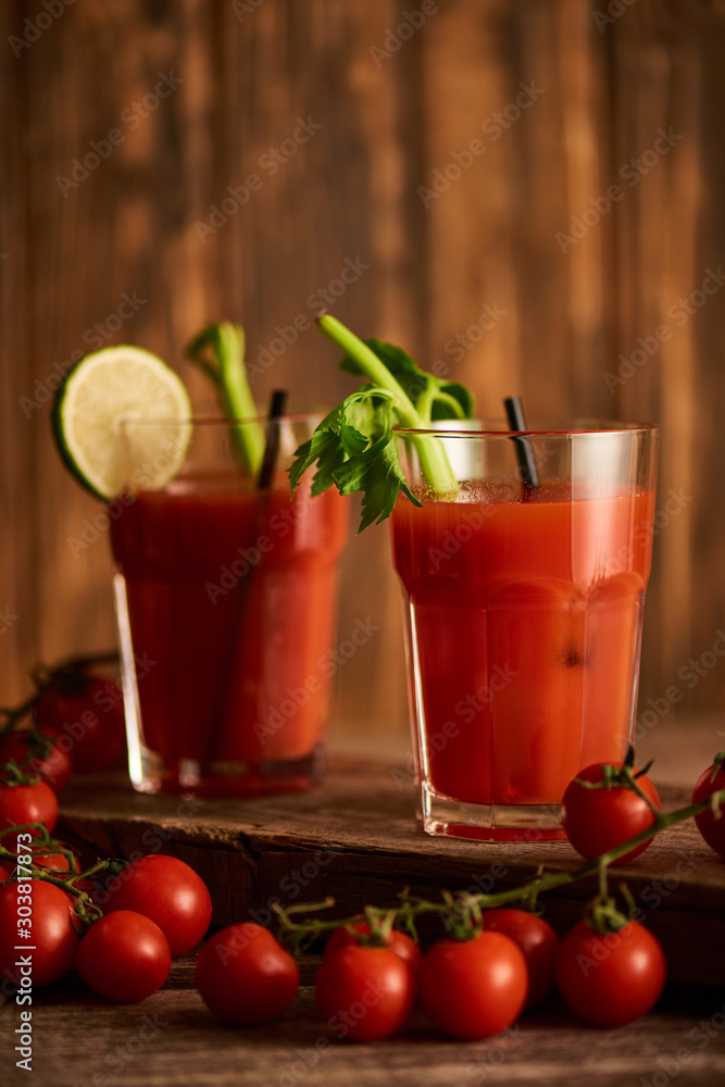 selective focus of bloody mary cocktail in glasses with lime and celery on wooden background with tomatoes selective focus of bloody mary cocktail in glasses with lime and celery on wooden background with tomatoes