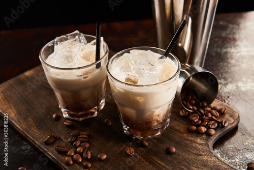 white russian cocktail in glasses with straws on wooden board with coffee grains photo