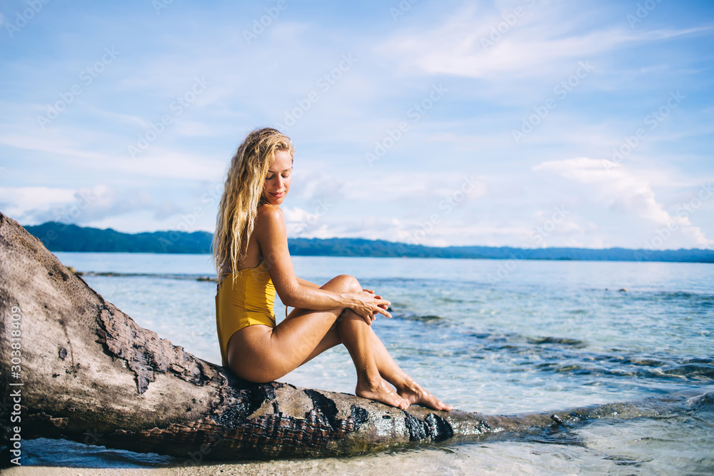 Young blonde sitting on dead tree on beach Young blonde sitting on dead tree on beach